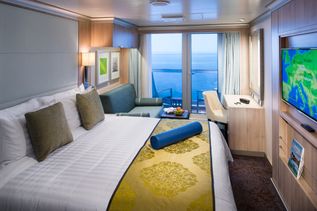 Eine moderne Kreuzfahrtkabine mit großem Bett, Sitzecke, Balkon und weitem Blick auf das Meer.