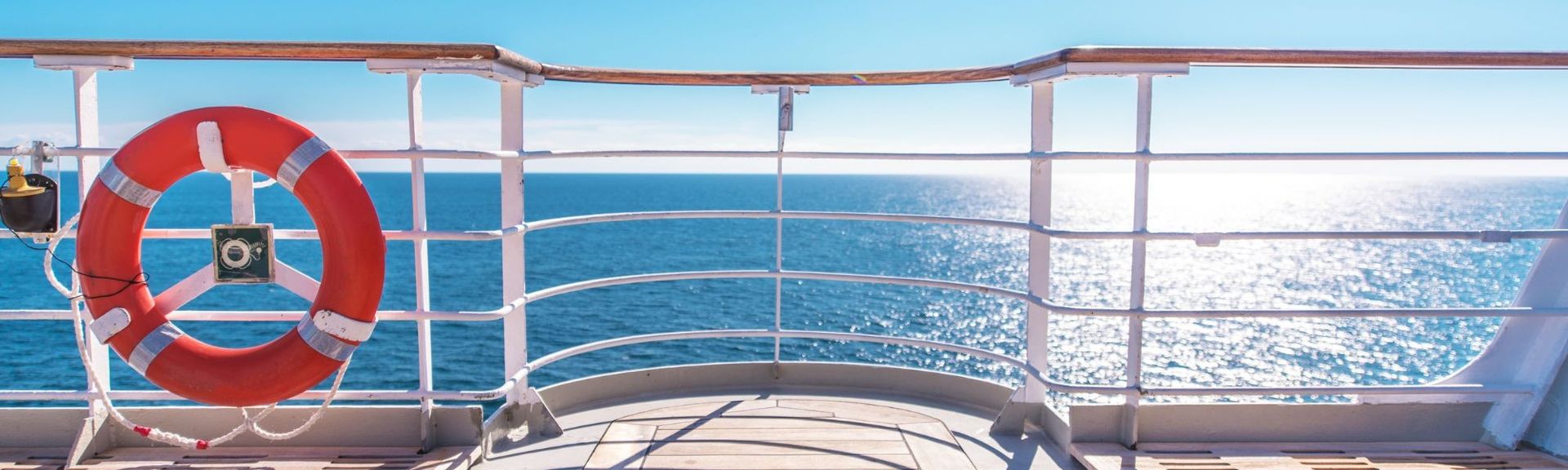 Blick vom Deck eines Kreuzfahrtschiffs auf das Meer mit blauem Himmel und rotem Rettungsring – Symbol für Reisen, Freiheit und Sicherheit auf See.