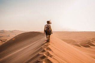 Frau mit Rucksack läuft auf dem Scheitel einer großen Sanddüne