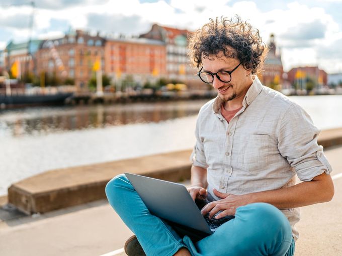 Mann mit Laptop am Kai vor der Stadtkulisse von Malmö in Schweden