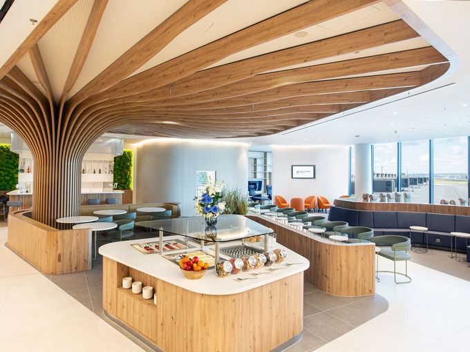SkyTeam Flagship Lounge Frankfurt mit geschwungener Holzdecke, zentralem Buffet, Sitzbereichen und Fensterblick aufs Rollfeld.