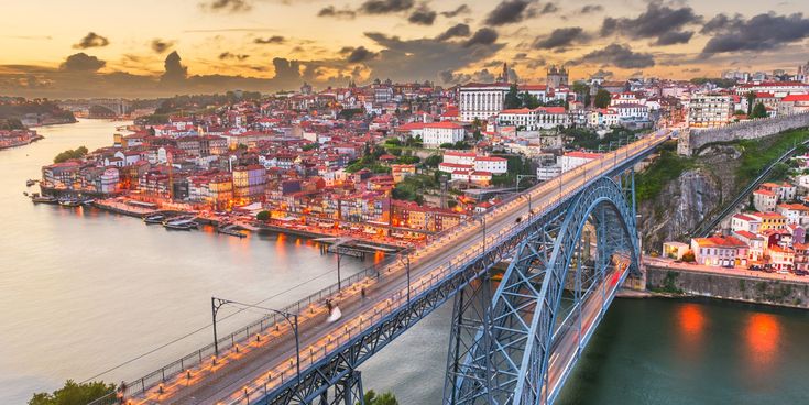 Blick auf die Stadt Porto bei Sonnenuntergang mit der Dom-Luís-I-Brücke über den Fluss Douro und den farbenfrohen Häusern der Altstadt.