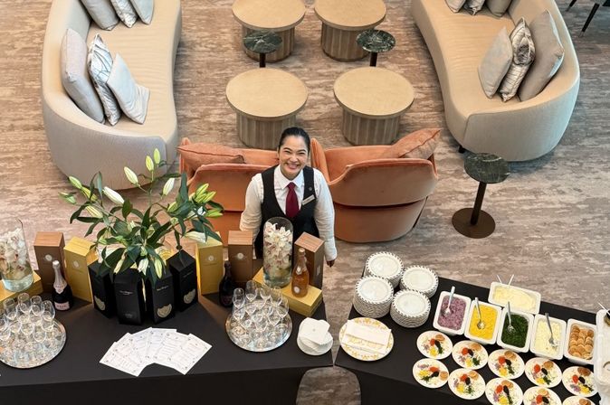 Mitarbeiterin steht lächelnd hinter einem Empfangsbuffet mit Champagner, Gläsern, Kaviar und Beilagen.