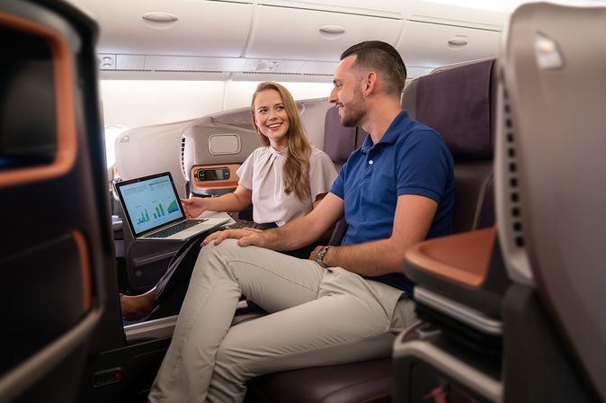 Geschäfsreisende in der Business Class von Singapore Airlines blicken auf einen Laptop Screen vor ihnen