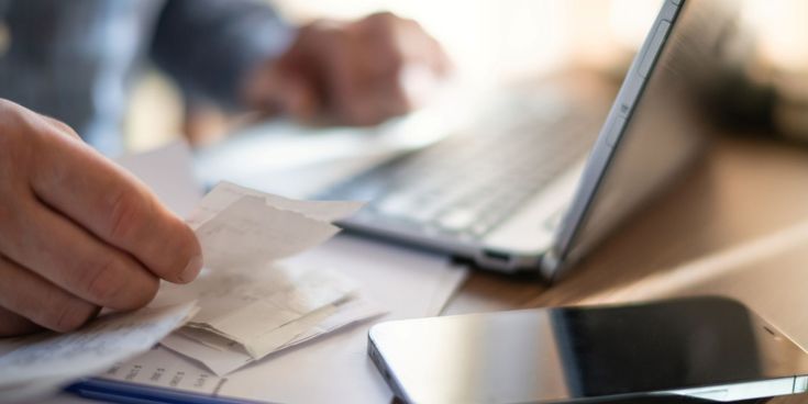 Geschäftsreisender prüft Belege neben Laptop und Smartphone
