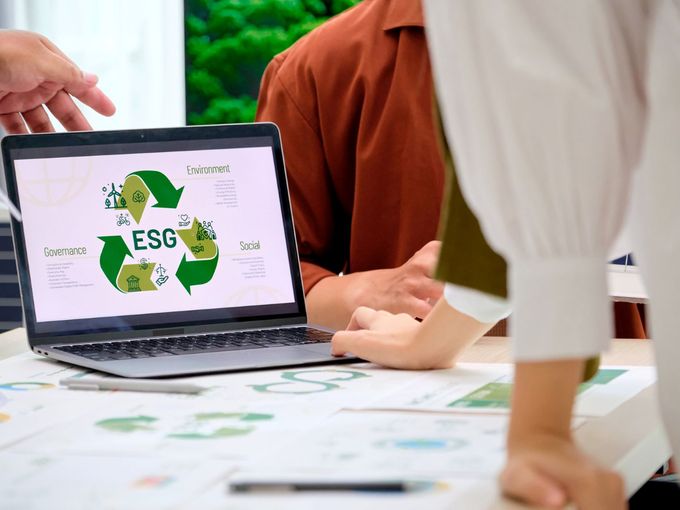 Laptop zeigt ESG-Grafik (Environment, Social, Governance) während eines Meetings mit mehreren Personen am Tisch.