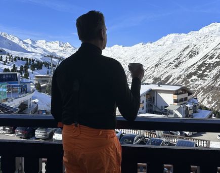 Ein Mann blickt von einem Hotelbalkon auf die verschneiten Berge von Hochgurgl.