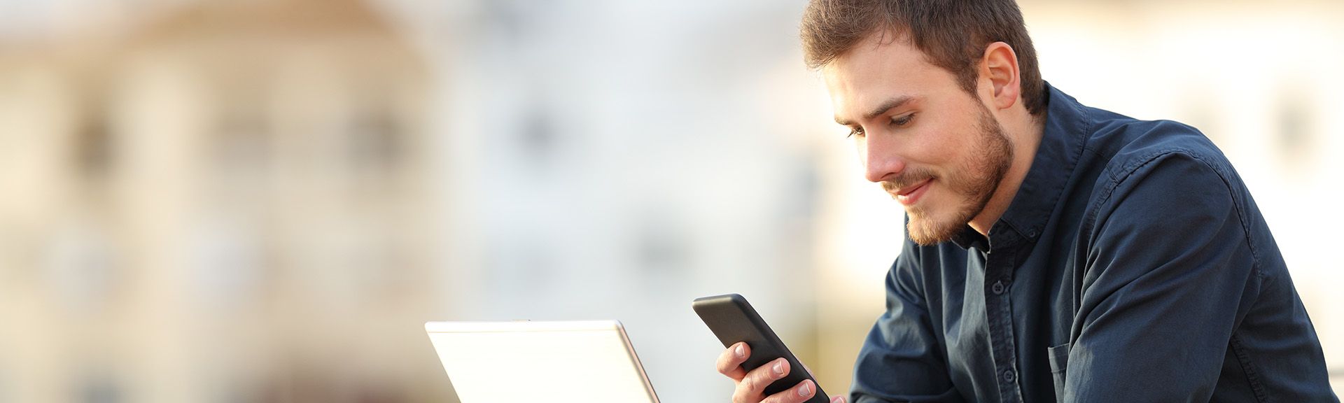 Mann mit Handy und Laptop an Mauer stehend