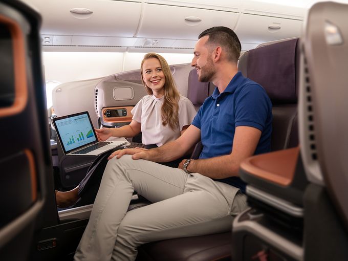 Geschäfsreisende in der Business Class von Singapore Airlines blicken auf einen Laptop Screen vor ihnen