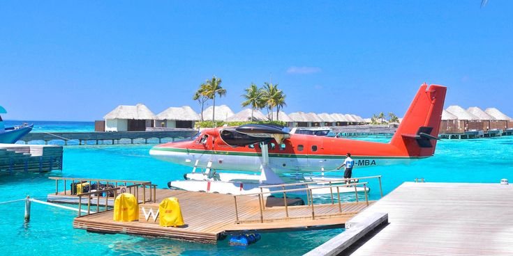 Rotes Wasserflugzeug an Holzsteg in türkisblauem Wasser vor Overwater-Bungalows auf den Malediven bei strahlendem Sonnenschein.