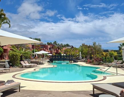 Geschwungener Hotelpool mit Sonnenliegen, weißen Schirmen und üppiger Gartenanlage.