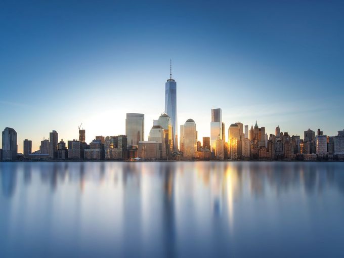 Skyline von New York mit One World Trade Center bei Sonnenuntergang, Spiegelung im Wasser.