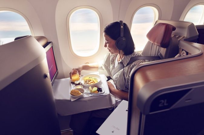 Passagierin sitzt an Bord von LATAM Airlines an einem Fensterplatz in der Business Class und erhält eine Mahlzeit am Sitz.