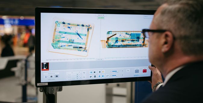 Sicherheitsbeamter am Flughafen Frankfurt schaut auf Screen und prüft Handgepäck mit Hilfe von KI