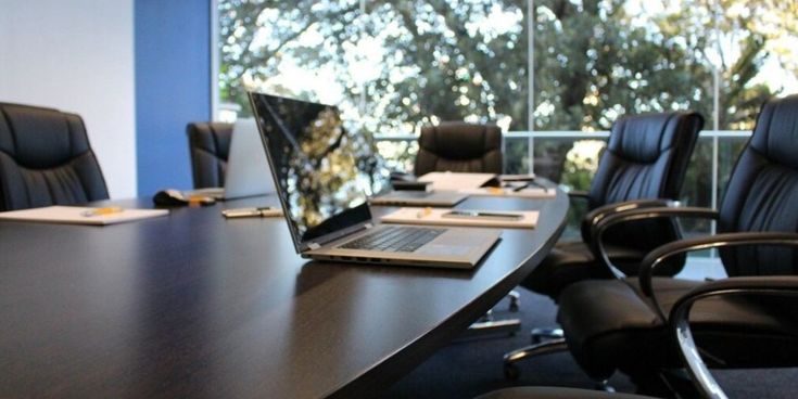 Moderner Konferenzraum mit Laptop und leeren Stühlen vor großen Fenstern – Sinnbild für professionelle Arbeitsumgebung und Geschäftsmeetings.