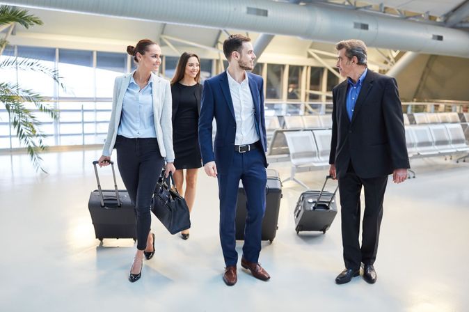 Gruppe von Geschäftsreisenden mit Rollkoffern unterhält sich beim Gehen durch die Flughafenhalle