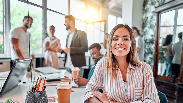 Lachende Frau im alternativen Büro mit Kaffeebecher und Kollegen