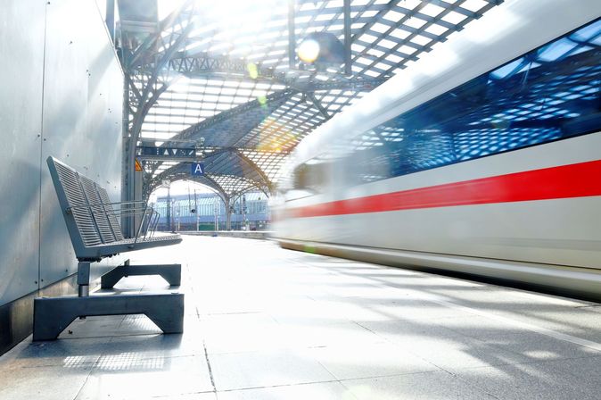 ICE-Zug fährt mit Bewegungsunschärfe in einen lichtdurchfluteten Bahnhof ein.