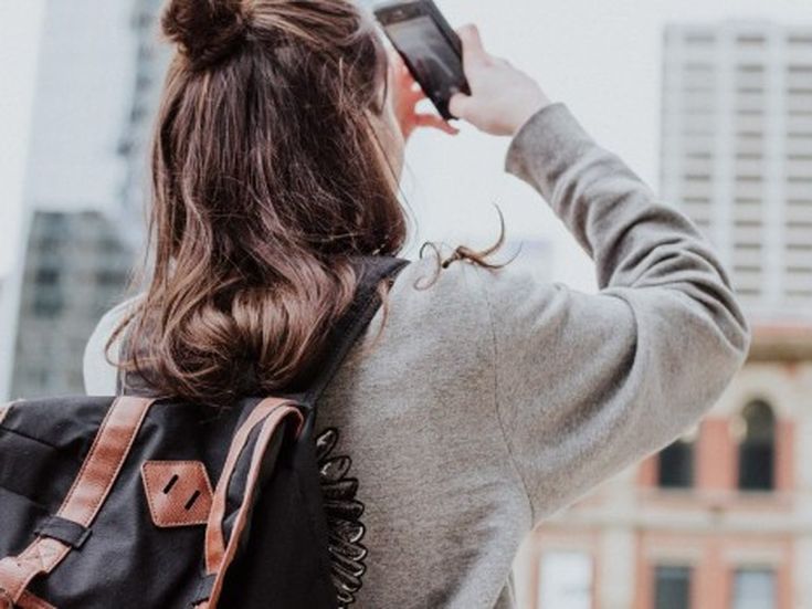 Frau mit Rucksack fotografiert Stadtarchitektur – moderner Städtetrip und digitale Reiseinspiration.