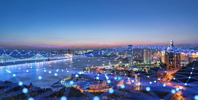 Stadtpanorama bei Nacht mti Skyline, Fluss und Brücke, beleuchtet und einzelnen blauen Lichtpunkten verbunden durch Linien für ein Netzwerk