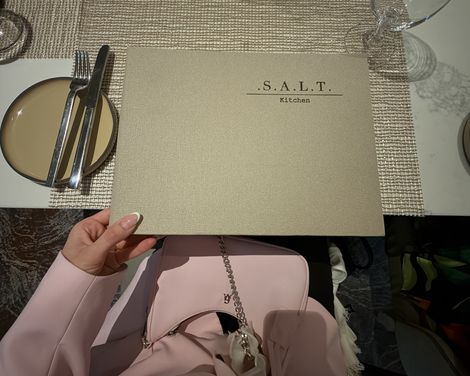 Marie Castor hält die Speisekarte des Restaurants S.A.L.T. Kitchen über einem gedeckten Tisch.