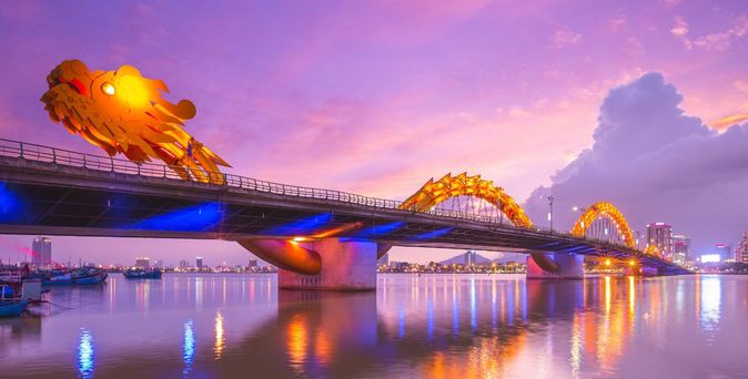 Beleuchtete Drachenbrücke in Da Nang bei Sonnenuntergang über dem Wasser