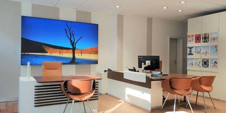 Beratungsplatz im Reisebüro mit großem Bildschirm, der eine Wüstenlandschaft zeigt, und moderner Einrichtung in warmen Farbtönen.