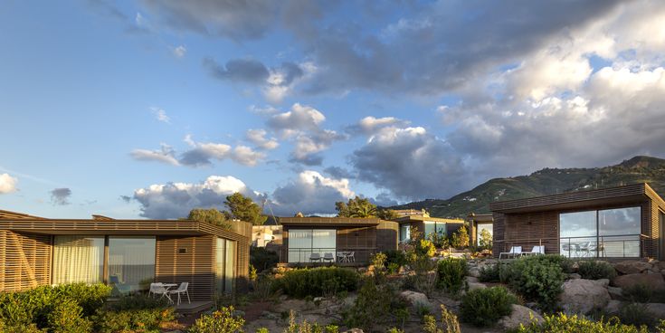 Moderne Holzvillen des Club Med Cefalù liegen in mediterraner Landschaft mit Blick auf das Meer – Symbol für nachhaltigen Luxus und Naturverbundenheit.