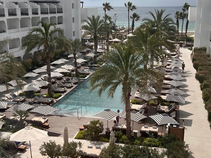 Blick über eine Hotelanlage mit Pool, Palmen und gestreiften Sonnenschirmen bis zum Meer.