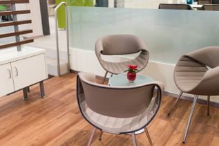 Moderner Wartebereich mit Designstühlen und kleinem Glastisch, auf dem eine rote Vase mit Blume steht – einladende Atmosphäre in einem Reisebüro.