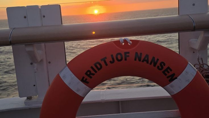 Sonnenuntergang über dem Meer, aufgenommen vom Deck der Fähre „Fridtjof Nansen“, mit rotem Rettungsring im Vordergrund.