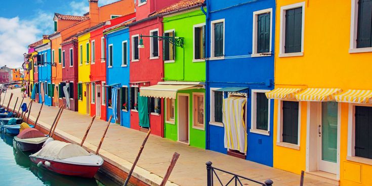 Bunte Häuserfassaden auf der Insel Burano bei Venedig, Italien, mit Booten am Kanal unter blauem Himmel.