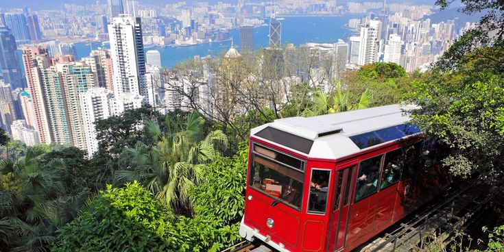 Blick vom Victoria Peak auf die Skyline von Hongkong mit Hochhäusern, dem Victoria Harbour und einer roten Standseilbahn im Vordergrund.