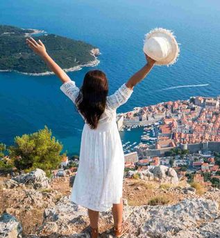 Eine Frau steht auf einem Aussichtspunkt über der Altstadt von Dubrovnik und blickt auf das Meer und die Stadtmauern Kroatiens.