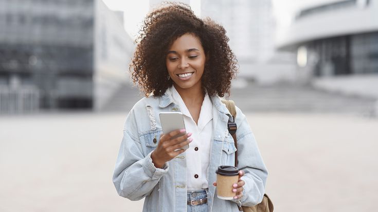 Frau mit Kaffeebecher und Handy auf Platz