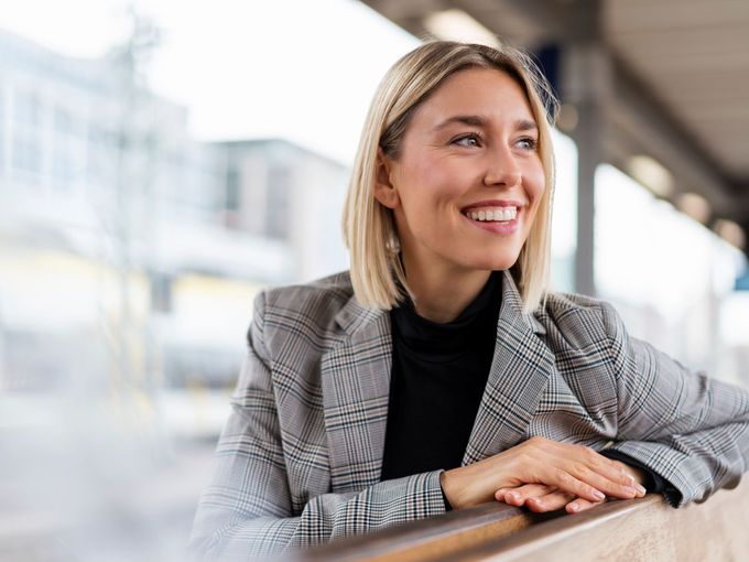 Frau sitzt auf einer Bank am Bahnhof und lächelt in die Kamera