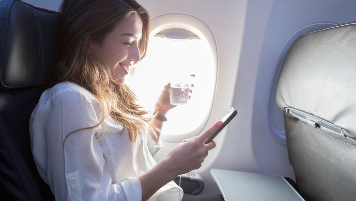 Frau mit Wasserglas und Handy im Flugzeug