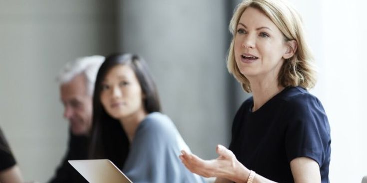Frau in einem Meeting spricht und gestikuliert, während Kolleg:innen zuhören – Symbol für Kommunikation, Führung und Zusammenarbeit im Business.
