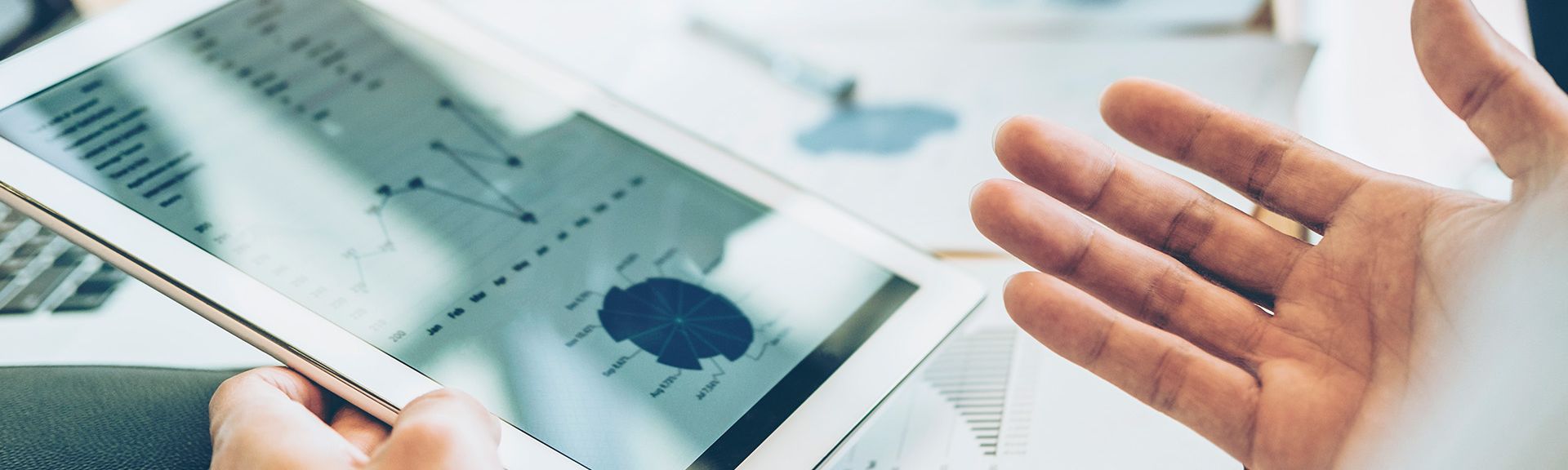 Tablet mit Kennzahlen und gestikulierenden Händen