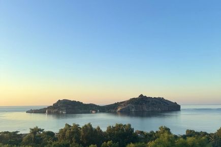 Insel mit bewaldeten Hügeln im ruhigen Meer unter klarem Himmel bei Sonnenaufgang oder Sonnenuntergang.
