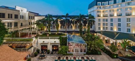 Weißes Hotel mit Bäumen im Vordergrund und leichter Beleuchtung 