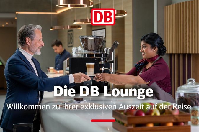 Person reicht an einer Theke in der DB Lounge einen Kaffee; im Hintergrund ist das DB‑Logo zu sehen.