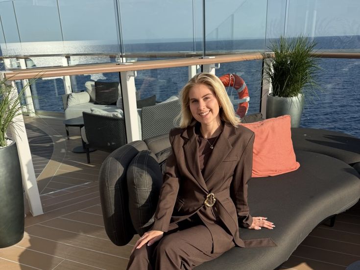 Marie Castor sitzt lächelnd in einem braunen Hosenanzug auf einer Sonnenliege an Deck der Silver Ray, das Meer im Hintergrund.