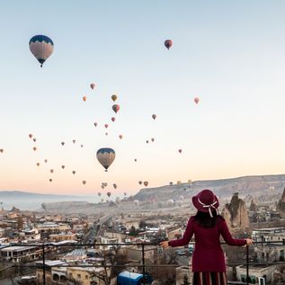 Frau blickt über eine Landschaft, die von hunderten bunten Heißluftballons überflogen wird