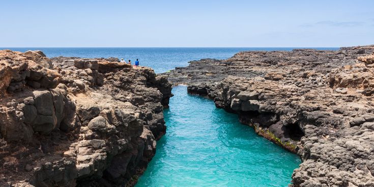 Felsküste auf der Insel Sal mit türkisblauem Meerwasser, das sich zwischen dunklen Lavagesteinsformationen hindurchschlängelt, unter klarem blauem Himmel.