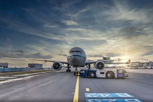 Ein Flugzeug wird bei Sonnenaufgang auf dem Rollfeld eines Flughafens von einem Pushback-Fahrzeug bewegt.