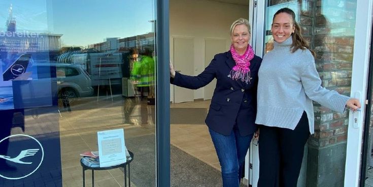 Zwei Frauen stehen lächelnd im Eingangsbereich eines neuen Bürostandorts mit Lufthansa City Center Logo – Symbol für erfolgreiche Standorteröffnung.