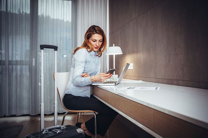 Geschäftsreisende nutzt Laptop und Smartphone im Hotelzimmer