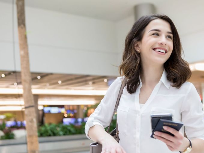 Eine lächelnde Frau steht im Flughafen mit Bordkarte und Reisepass in der Hand.