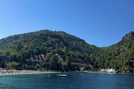 Bucht mit klarem blauem Wasser, bewaldeten Hügeln und Gebäuden am Ufer unter blauem Himmel.